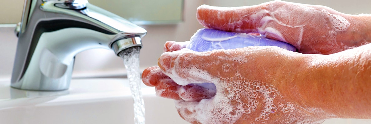 a man's hands being washed under a home faucet with soap and running water