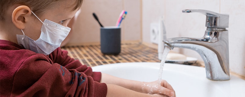 Image of a boy with a mask washing his hands at school