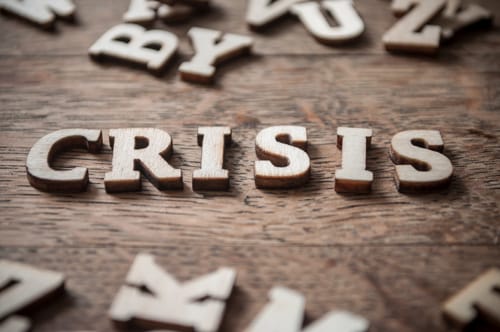 Wooden letters spelling out the word crisis on a board surrounded by random letters.