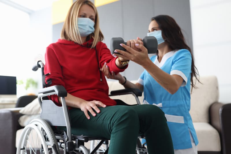 health care worker wearing face mask assisting woman in wheelchair also wearing face mask