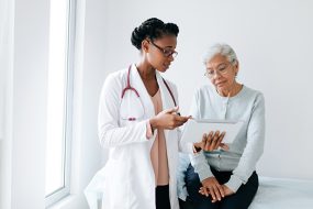 Black female doctor showing digital tablet to senior patient