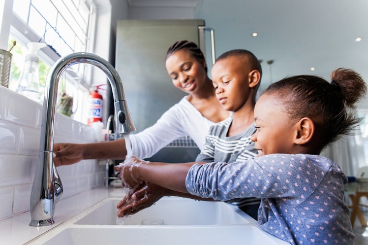 Family washing their hands together as the mom supervises her children.