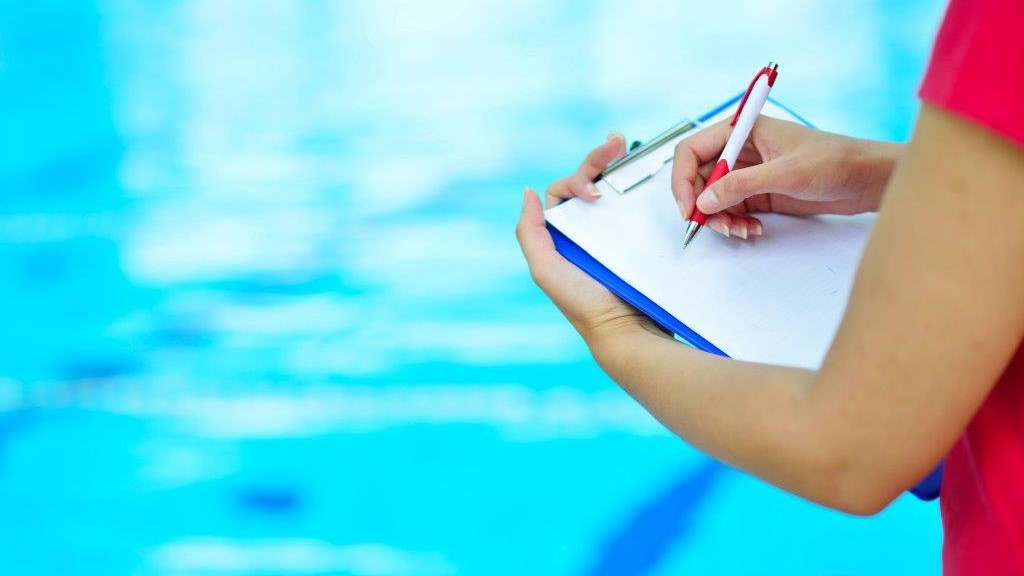 Photo of a woman with a clipboard standing in front of a pool.
