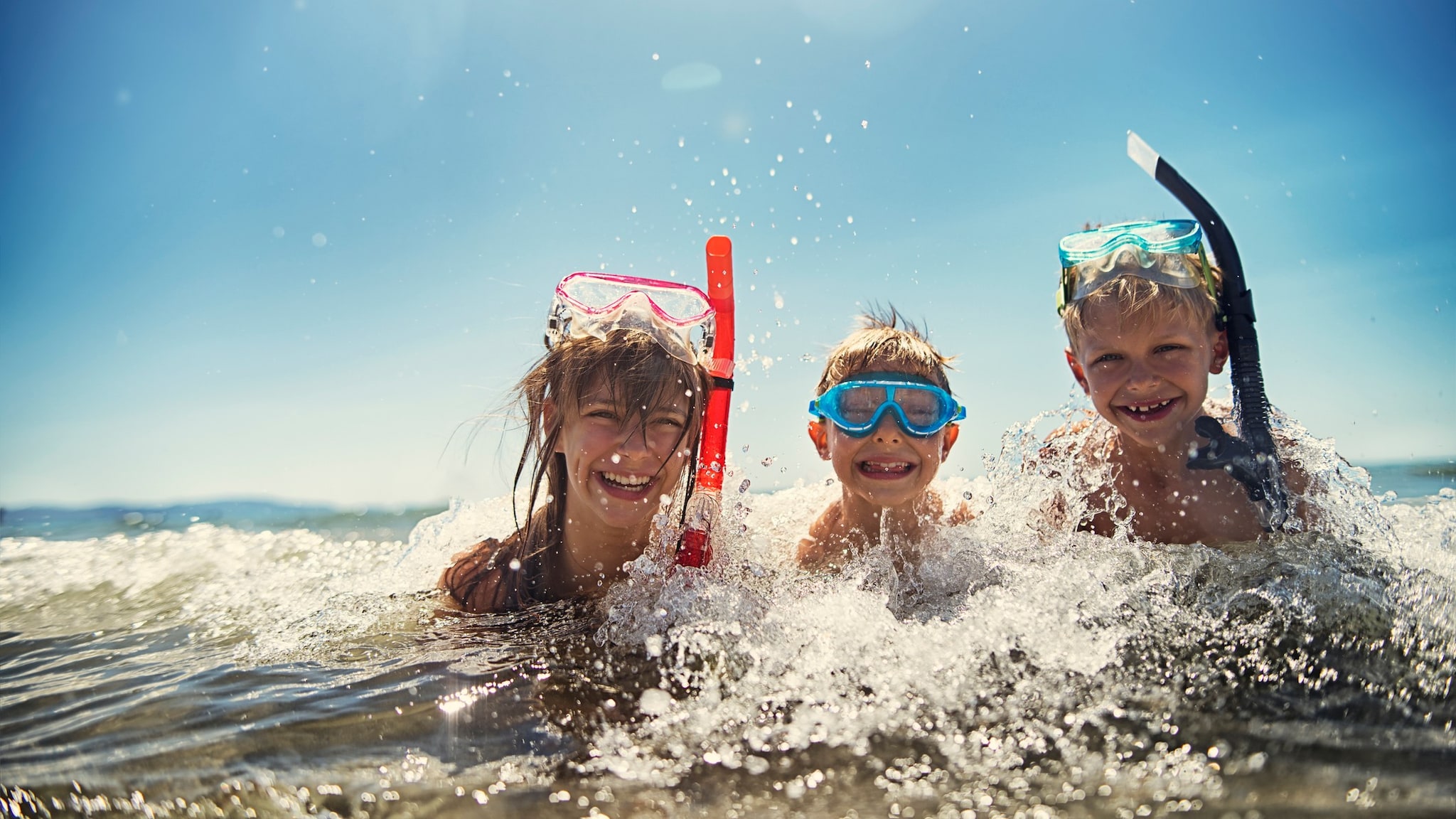 Three kids playing in the ocean together while wearing snorkels.