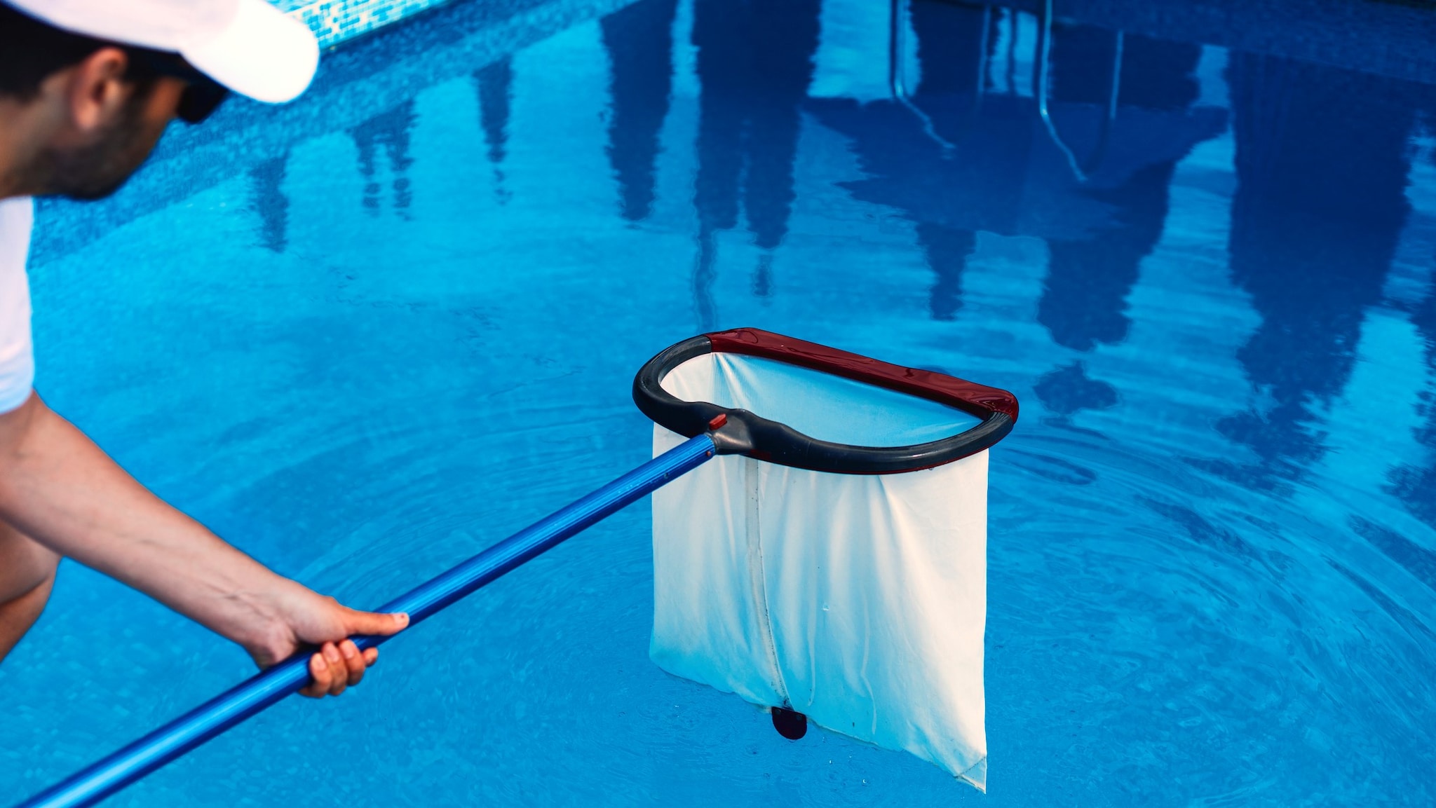 Man with a hat holding a pool net over a pool.