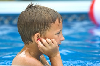 Young boy in the pool putting ear plugs in.