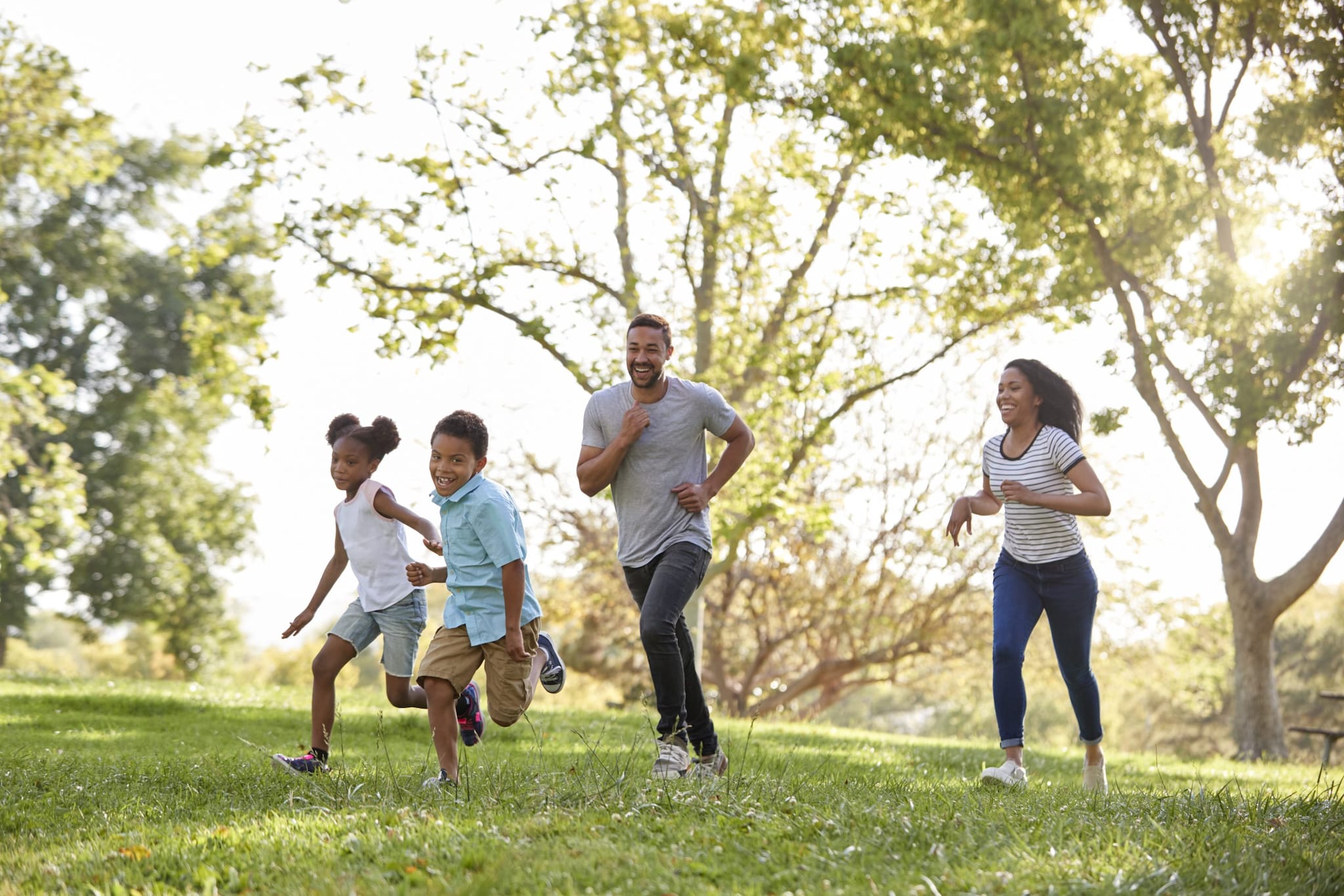 Family of two children and two adults run and play together outdoors.
