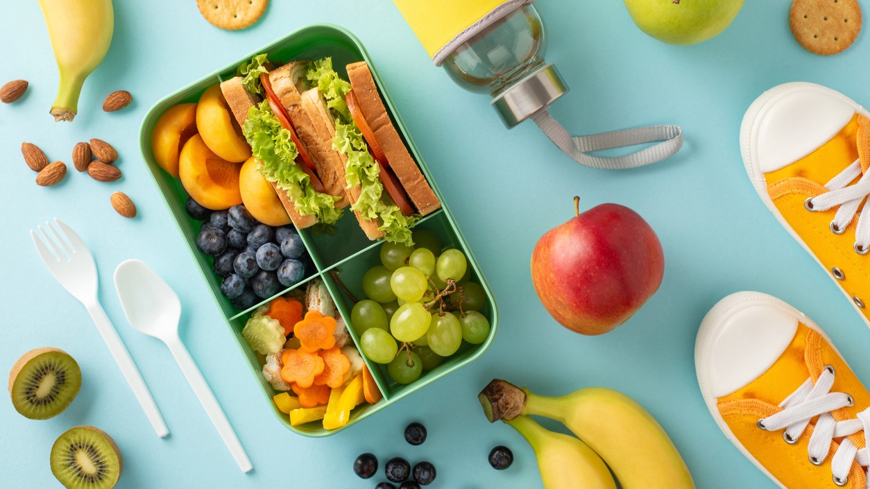 Lunch box with fruit next to tennis shoes and a water bottle.