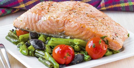 A plate of salmon on top of roasted peppers, tomatoes, and asparagus.