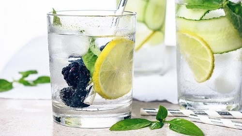 Glasses of water with lemon, cucumber, basil, and blackberry.