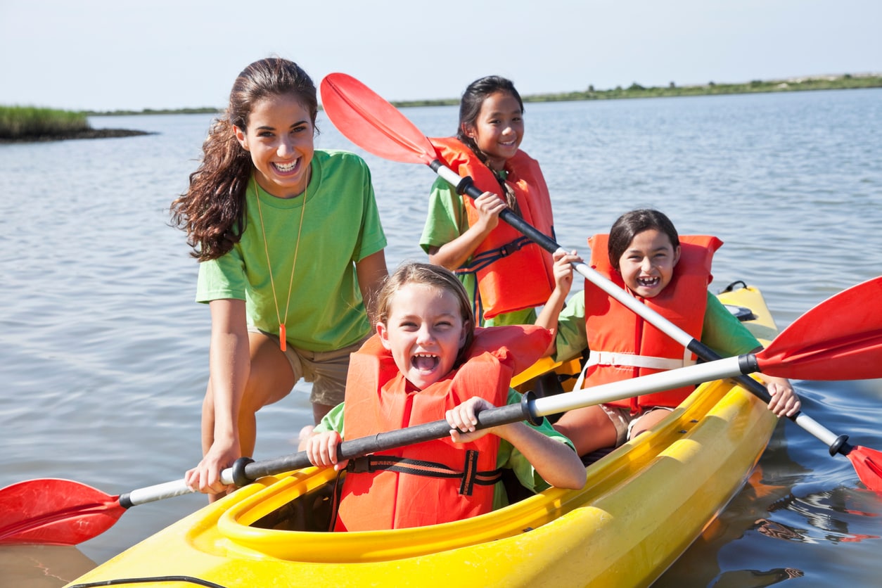 Teen camp counselor helping children in kayak.