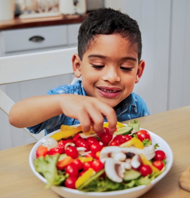 Un niño pequeño recogiendo verduras de un tazón en el mostrador de una cocina.