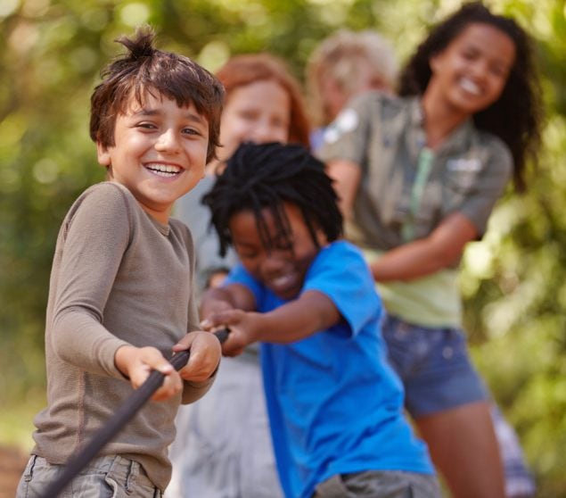 مجموعة من الأطفال الصغار متعددي الأعراق يلعبون لعبة شد الحبل بالخارج.