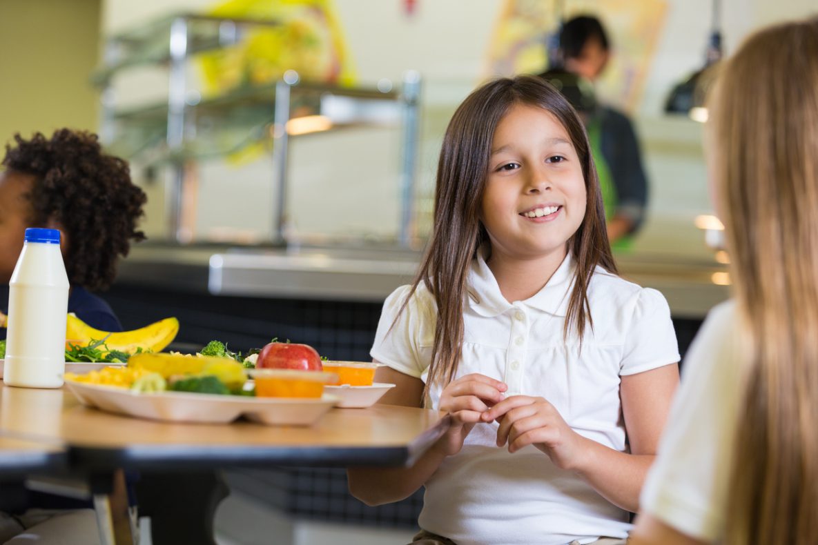 Elementary school girls eating healthy meal in cafeteria lunchroom.