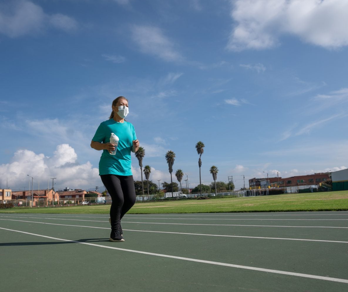 Adult woman exercising at the running track wearing a facemask