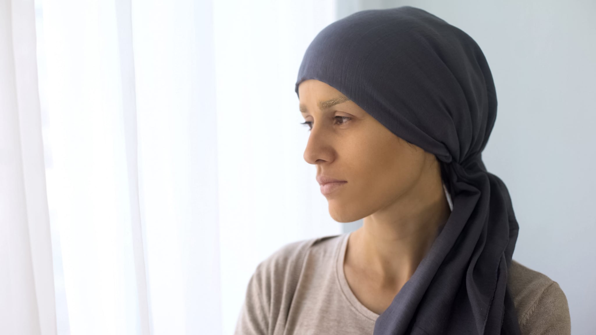 Photo of a woman with cancer, wearing a head covering, looking off into the distance.
