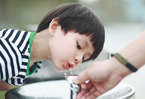 A boy drinking from an outdoor water fountain.