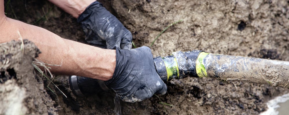 Image of a mans hands fixing an underground water pipe