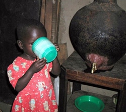 A young girl drinks safe water from a SWS storage vessel in her home.
