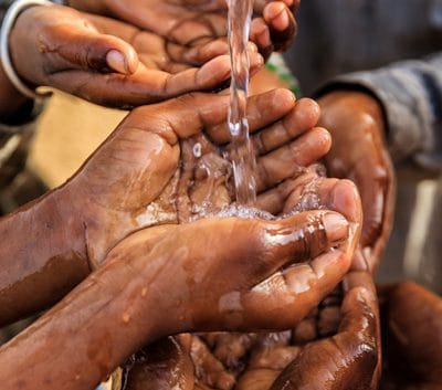 Close up of several hands being washed with clean water