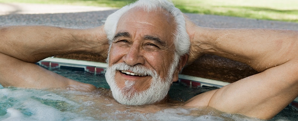 A middle-aged man at the edge of a hot tub with a relaxed smile