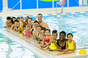 a diverse group of parents and children posing at a concrete island in the middle of a swimming pool