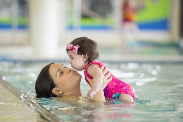 mother giving kisses to a toddler in a swimming pool