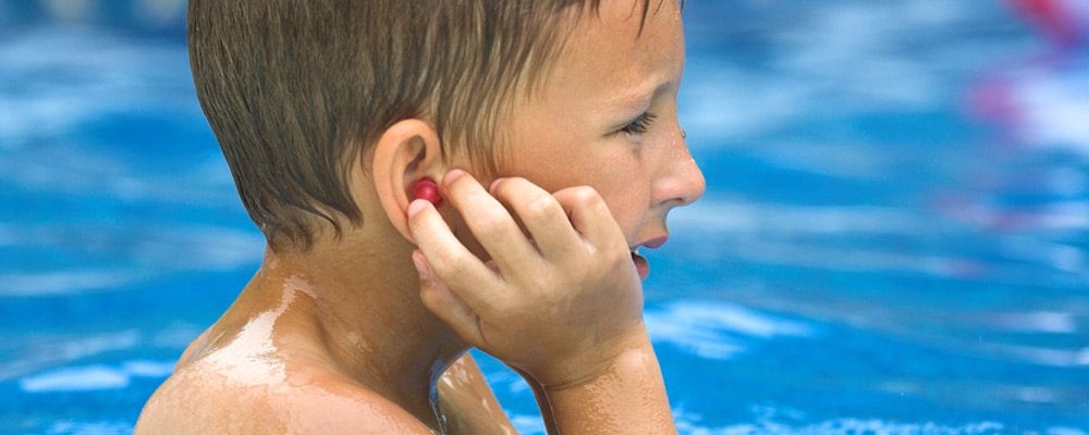 Close up image of a boy in the pool with ear plugs