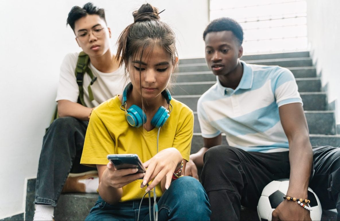Three teenagers African American and Asian High School friends watching smartphone together