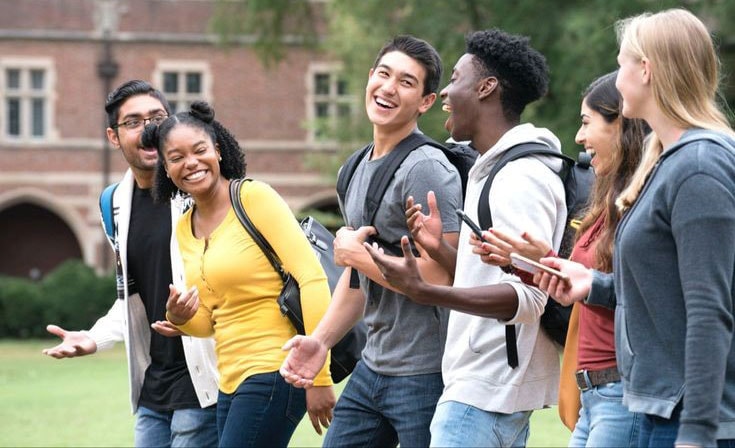 A group of teens smiling in front of school building