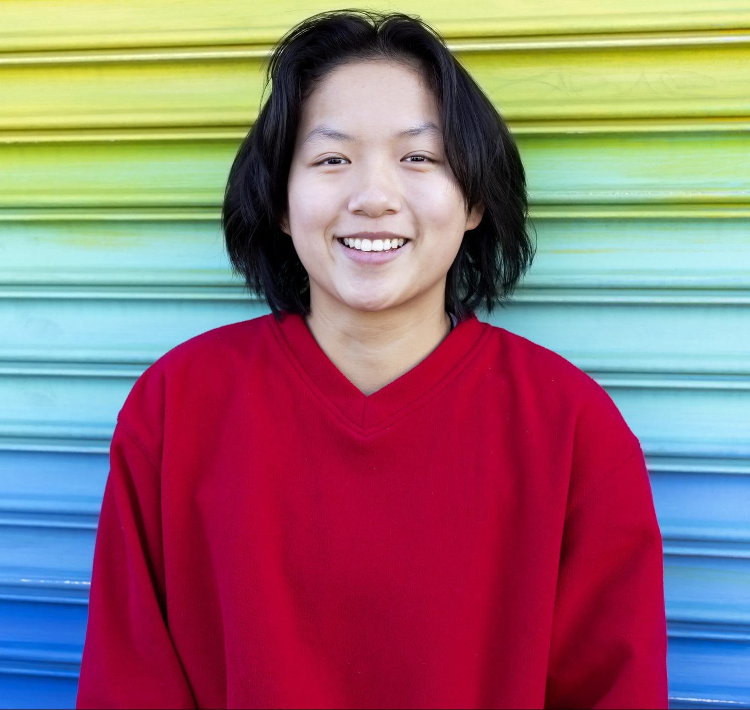 Smiling Asian teenager with LGBTQ colors in the back wall