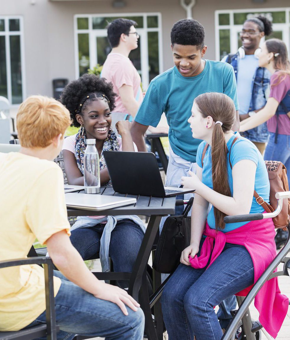 Group of diverse teenagers working together on a laptop, outside on the school patio