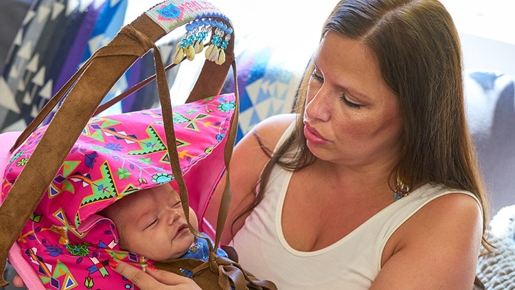 woman holding sleeping baby in pink cradleboard