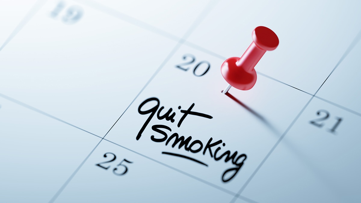 A calendar with "quit smoking" written on a date with a red pin next to it.