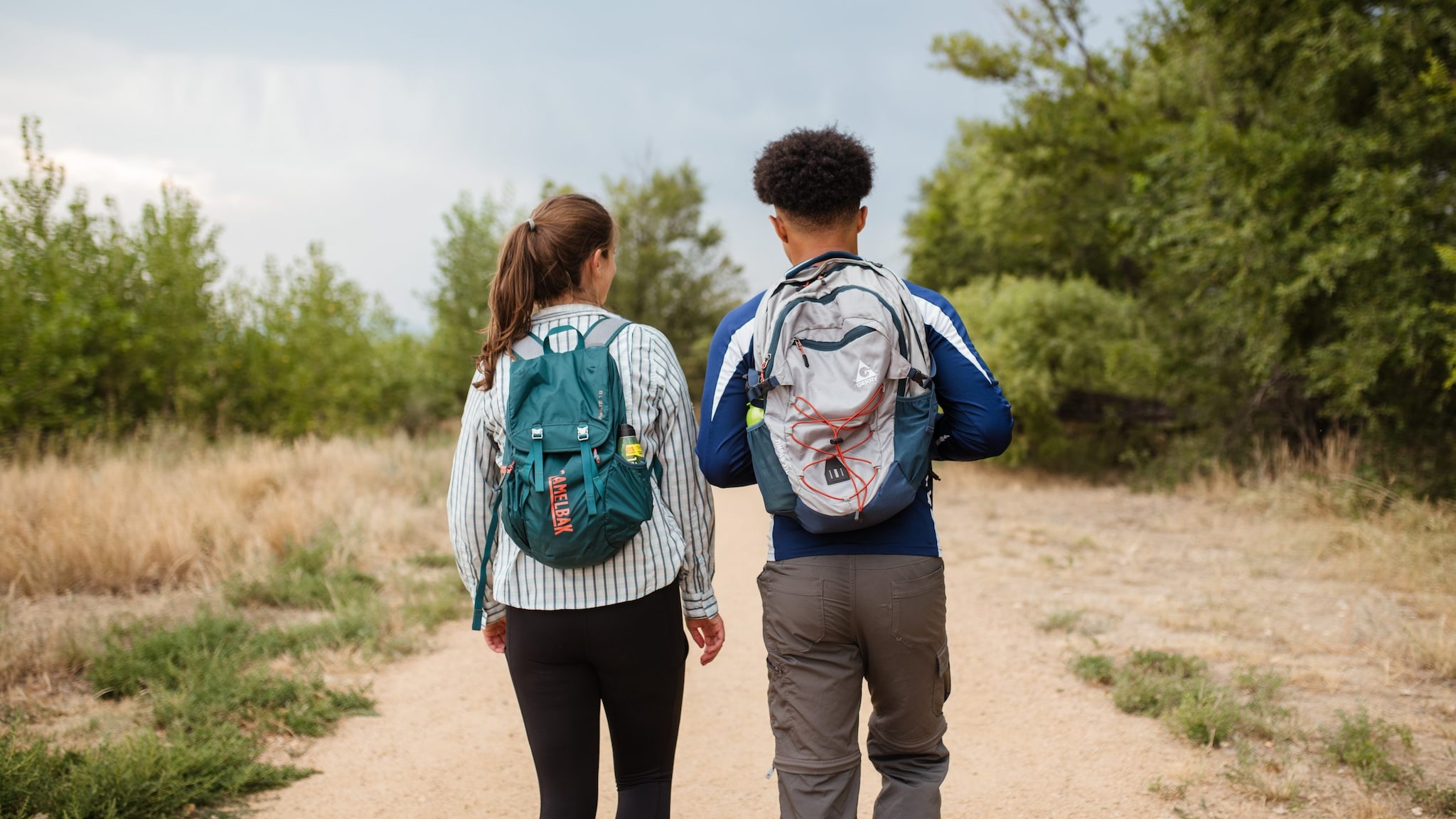 Two people walking on a trial with backpacks on.