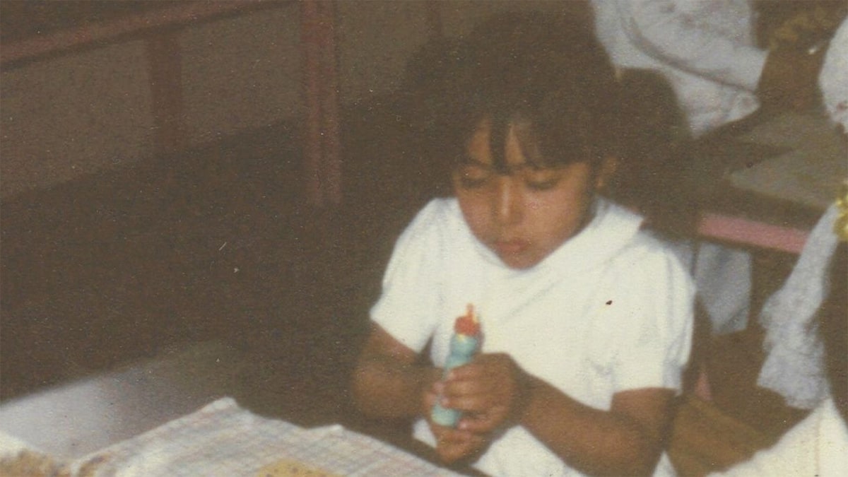 A young girl is sitting at a table gluing paper to make a craft.