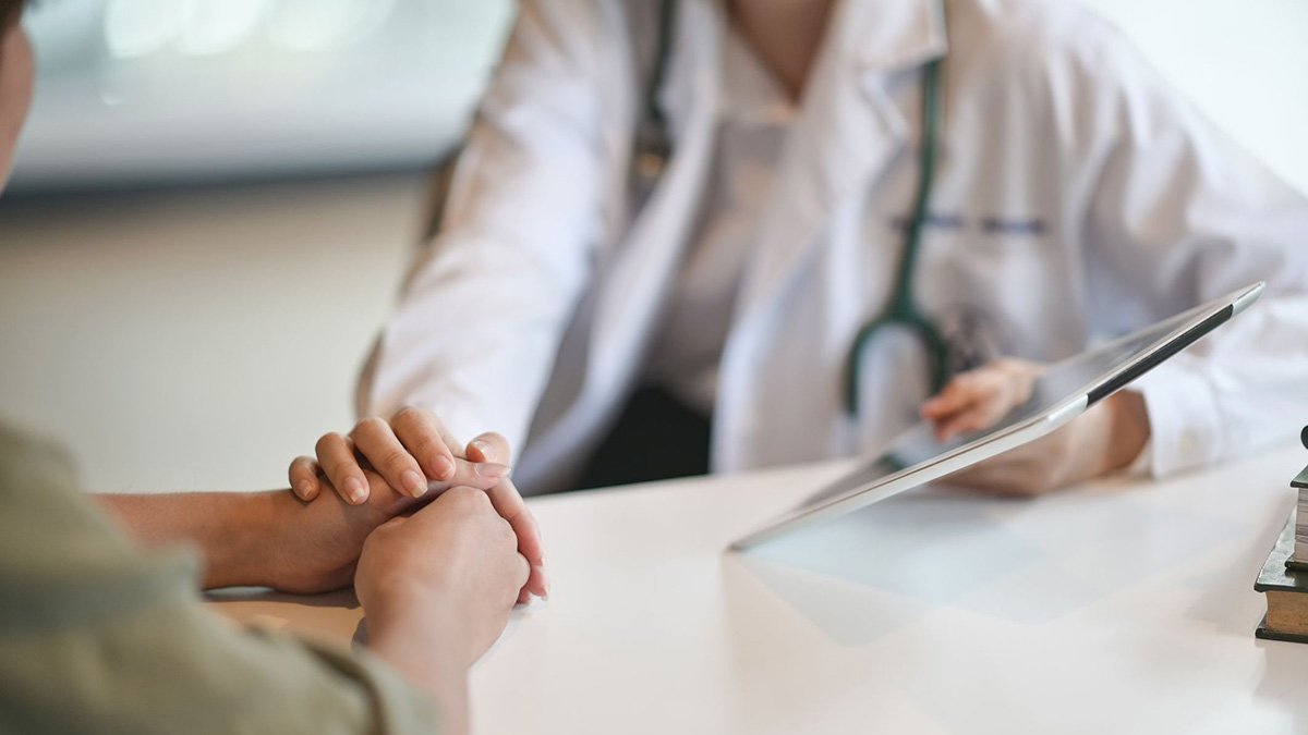 Lower body picture of a doctor showing information on a tablet to a patient