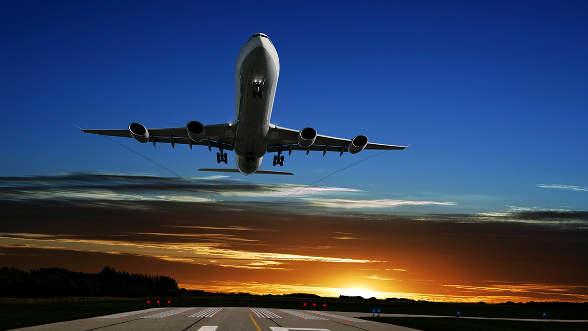 An airplane taking off a runway with the sunset in the background