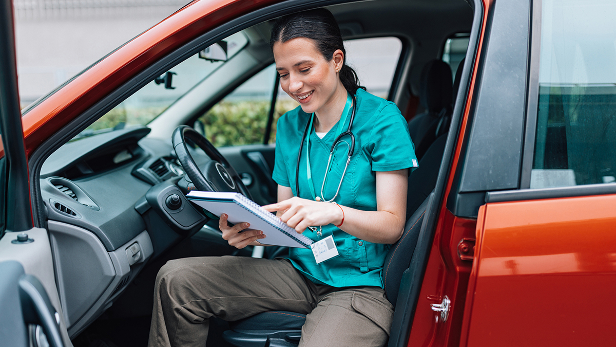 A healthcare professional getting out of her car while looking at her notebook