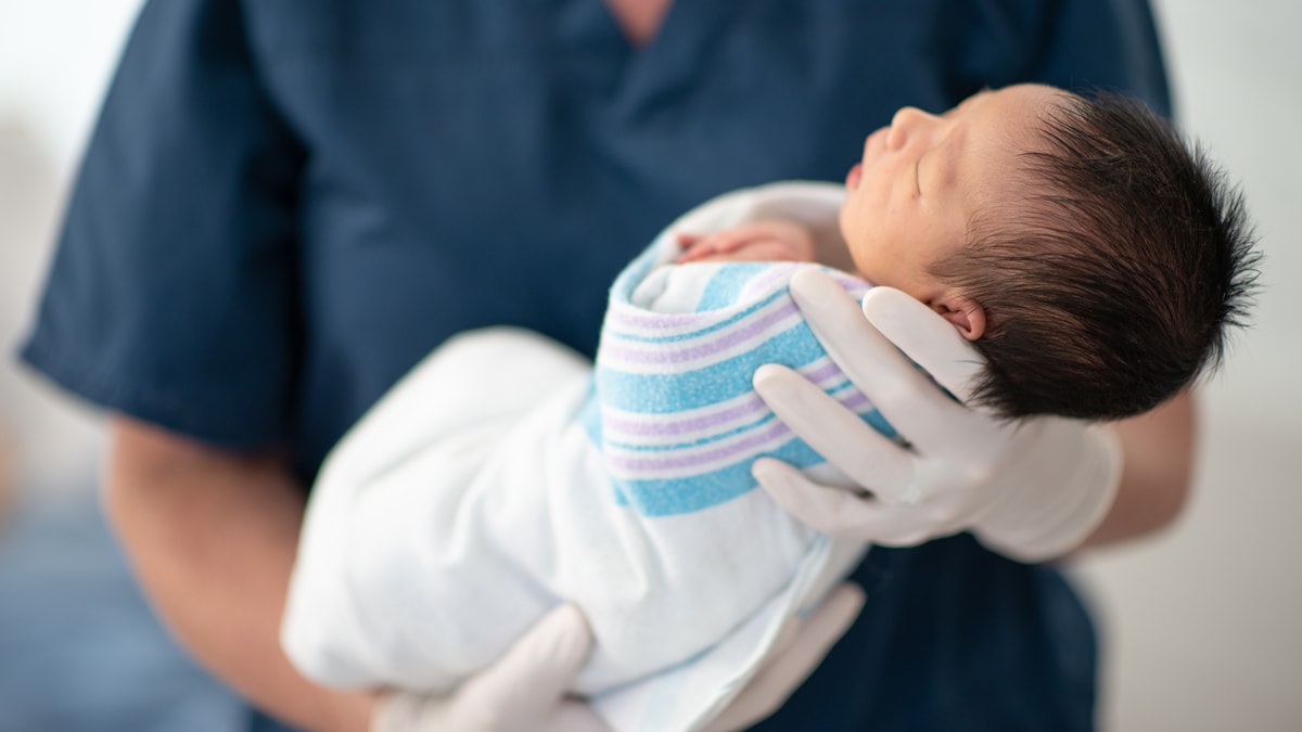 A healthcare professional holding a newborn baby wrapped in a blanket