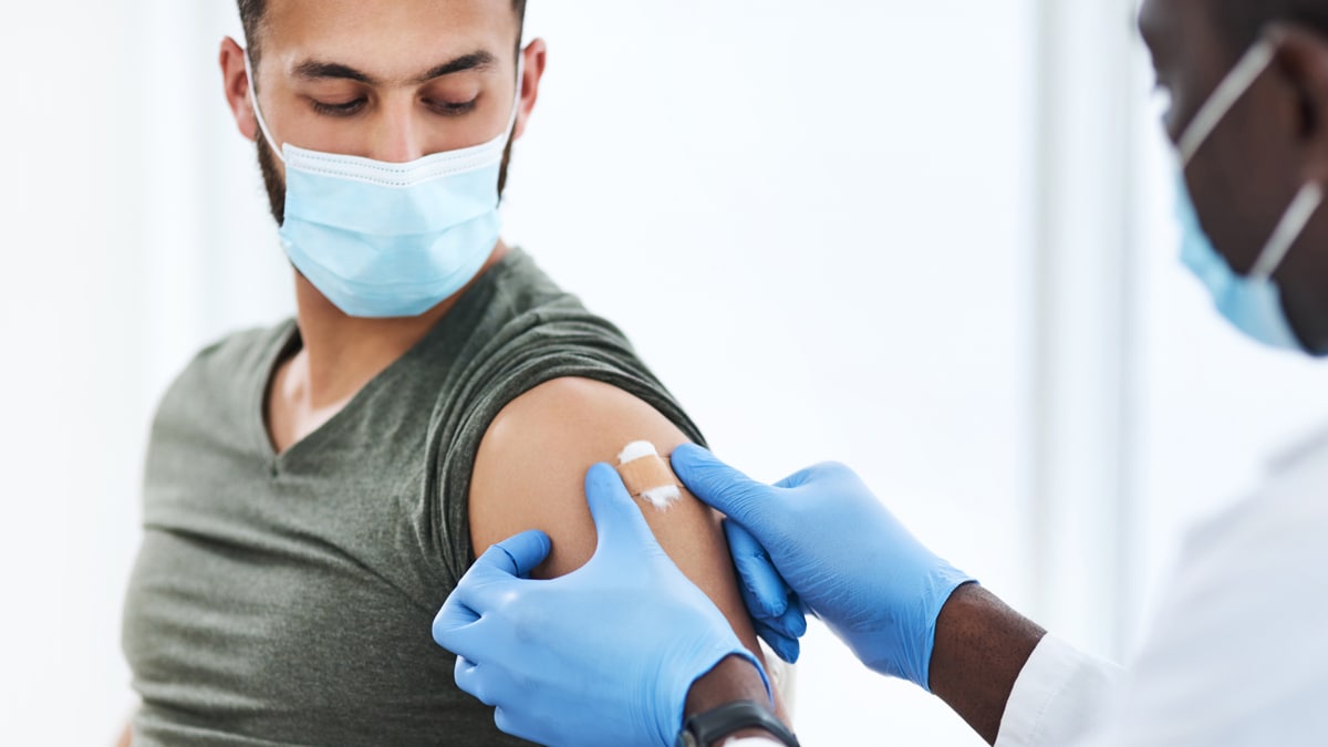 A doctor placing a bandage over the vaccination site on a patient's shoulder
