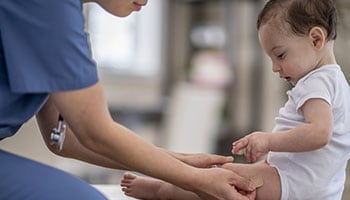 Médica poniéndole una curita en la pierna a un bebé.