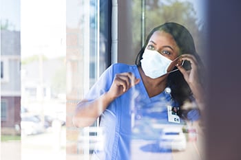 African American female healthcare worker dons a face mask as she approaches a healthcare facility