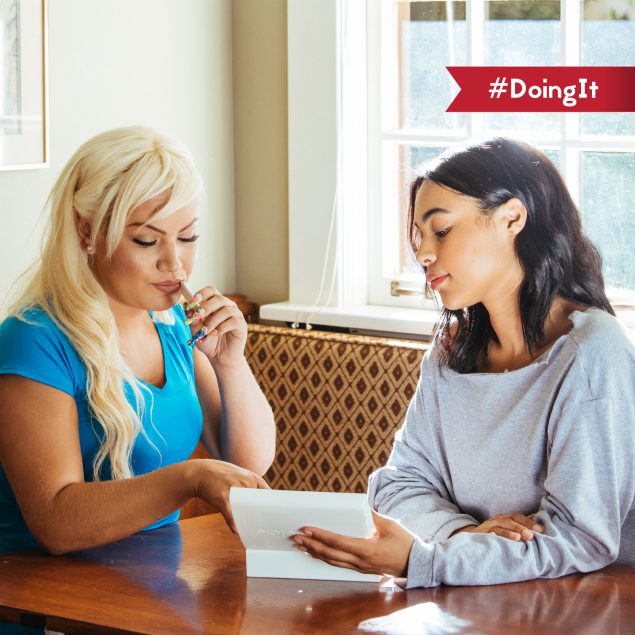 Two women sitting at a table looking at a piece of paper. One is taking an HIV self-test. #DoingIt