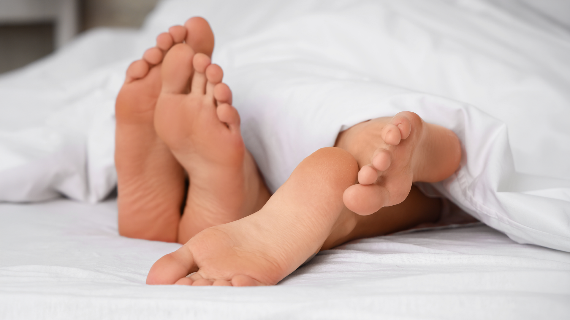Image of two pair of feet sticking out from under bed sheets.