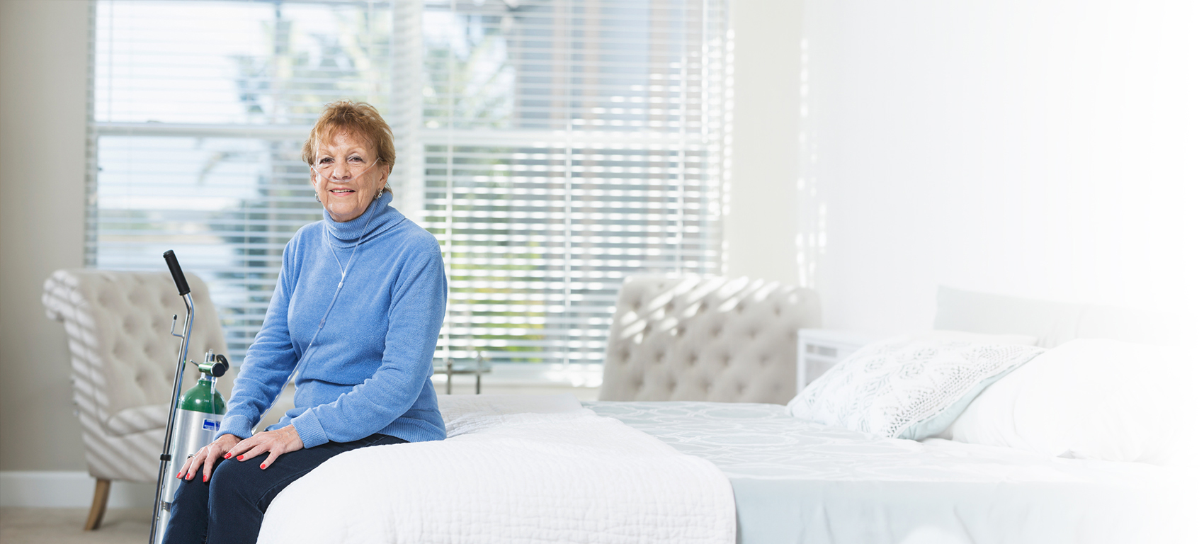 Older woman using supplemental oxygen while sitting on a bed