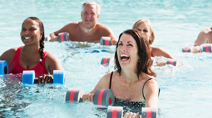 Group of people in swimming pool doing water exercises with foam weights