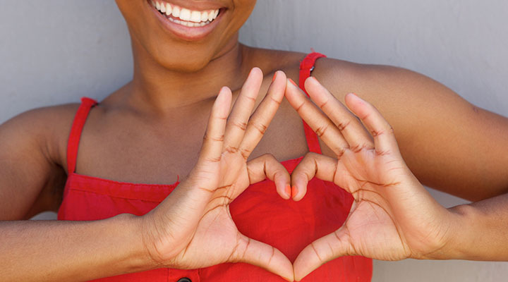 Woman making a heart sign with fingers over her heart and smiling