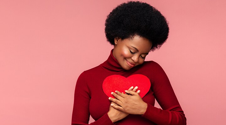 Woman holding a heart shape up to her chest and smiling
