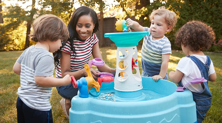 Teacher and young children playing outdoors with water toys